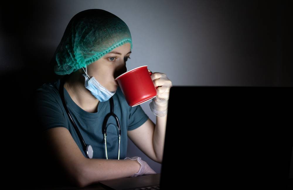 Night shift nurse drinking coffee and looking at a computer.